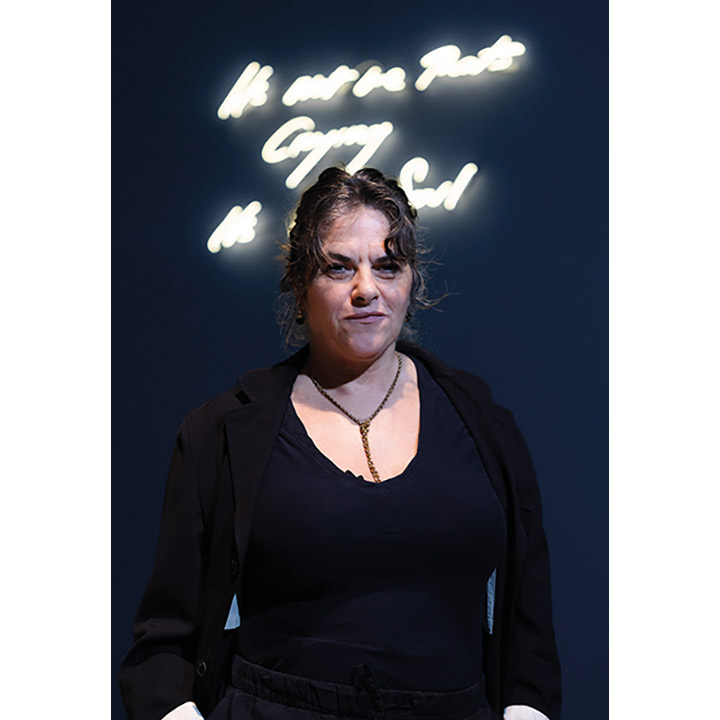 Portrait photograph of Tracey Emin stood against a blue background in Tate Modern